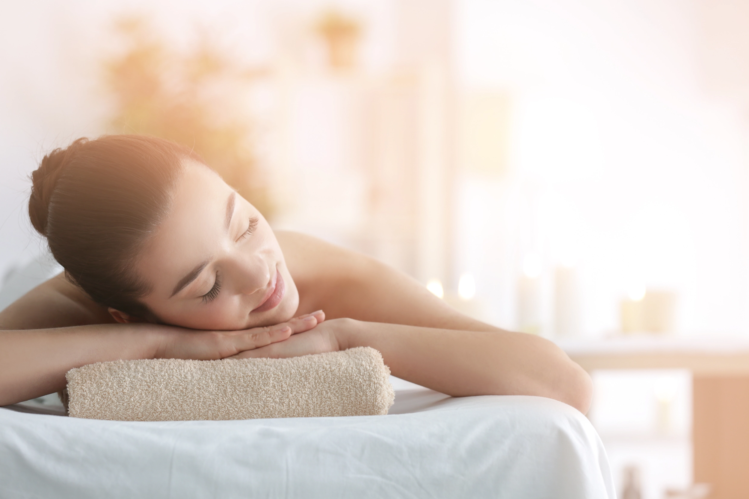 A woman relaxing face-down on a massage table in a bright, sunlit treatment room